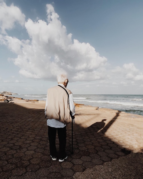 Hintergrundansicht eines älteren Mannes, der am Strand gegen den Himmel steht
