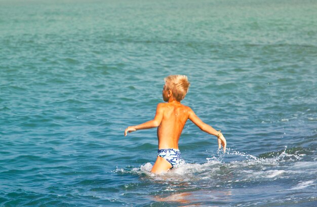 Hintergrundansicht eines hemdlosen Jungen, der gegen einen klaren Himmel im Meer schwimmt