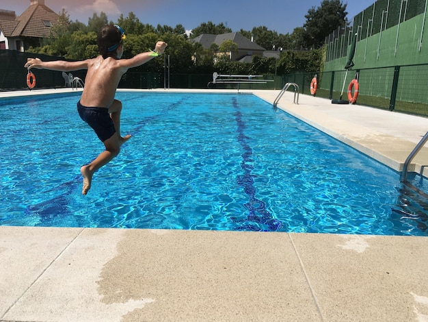 Hintergrundansicht eines hemdlosen Jungen, der im Schwimmbad im Resort springt