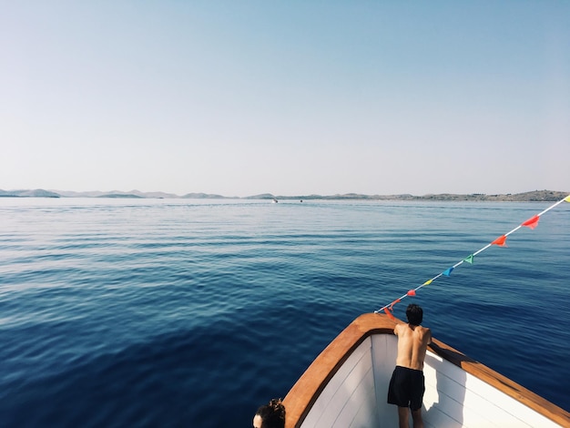 Foto hintergrundansicht eines hemdlosen mannes, der auf einem boot auf dem meer gegen einen klaren himmel steht