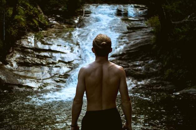 Hintergrundansicht eines hemdlosen Mannes, der gegen einen Wasserfall steht