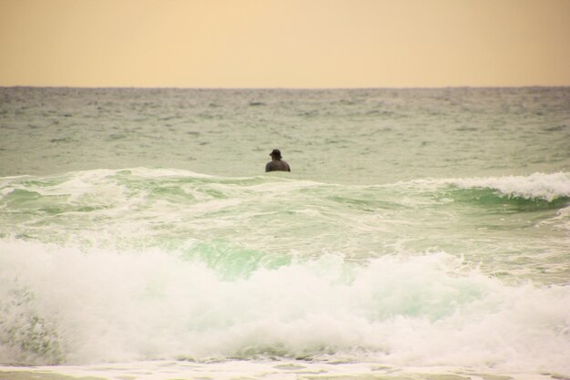 Hintergrundansicht eines hemdlosen Mannes, der im Meer gegen den Himmel steht