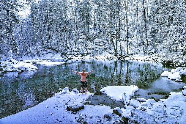 Hintergrundansicht eines hemdlosen Mannes, der im Winter am See im Wald steht