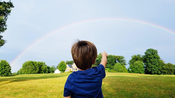 Foto hintergrundansicht eines jungen, der auf dem feld steht und auf den regenbogen zeigt
