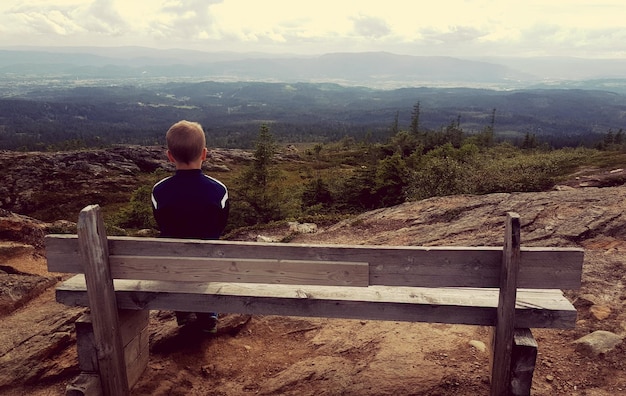 Foto hintergrundansicht eines jungen, der auf einer bank am berg gegen den himmel sitzt