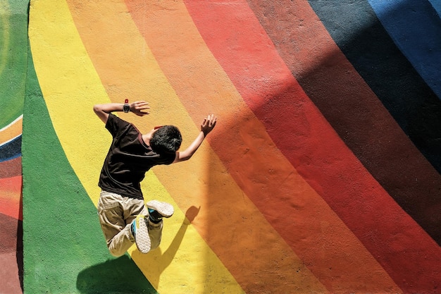 Hintergrundansicht eines Jungen, der gegen eine Regenbogenwand springt