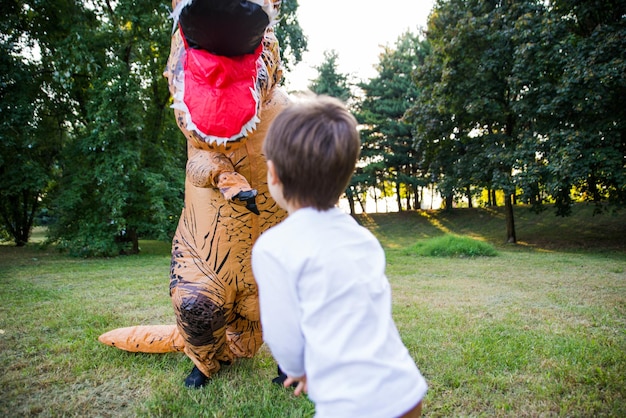 Foto hintergrundansicht eines jungen, der mit einer person im dinosaurier-kostüm im park spielt