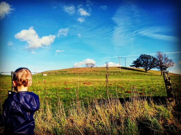 Hintergrundansicht eines Jungen in Regenmantel auf einem grünen Feld