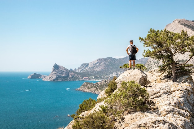 Hintergrundansicht eines jungen Mannes, der am Meer vor einem klaren Himmel auf einer Klippe steht