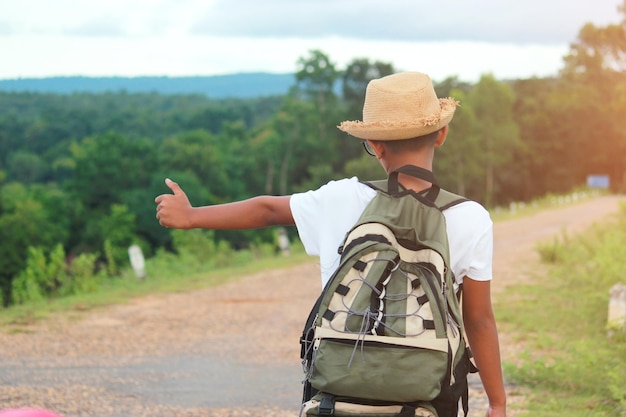 Foto hintergrundansicht eines jungen mit rucksack, der auf der straße steht und autostop macht