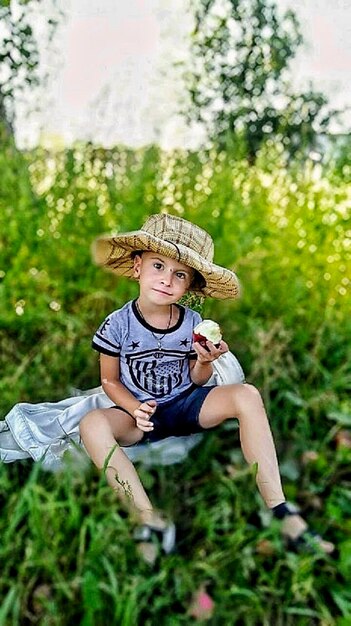 Hintergrundansicht eines kleinen Jungen, der auf einem grasigen Feld sitzt und einen Apfel isst