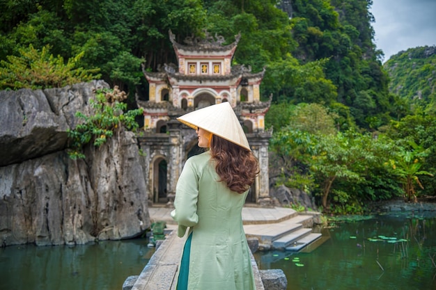 Foto hintergrundansicht eines mädchens, das ao dai trägt, vor einer außenparklandschaft mit see und steinbrücke. eingang zur alten bich dong-pagode-komplex ninh binh vietnam reiseziel