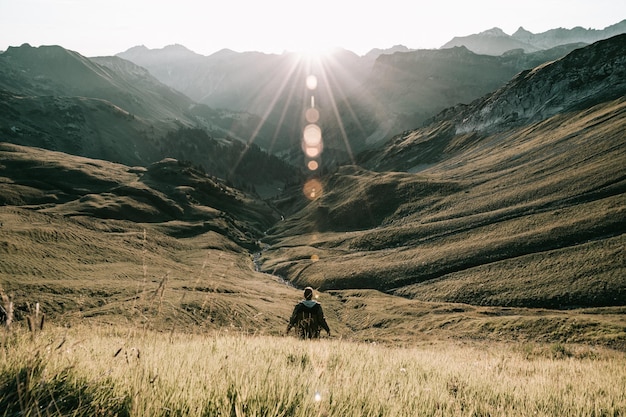 Hintergrundansicht eines Mannes, der am Gras gegen Berge steht