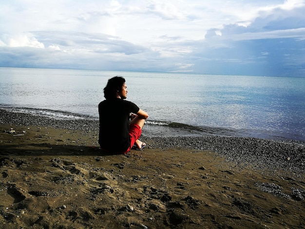 Foto hintergrundansicht eines mannes, der am strand auf dem ufer sitzt