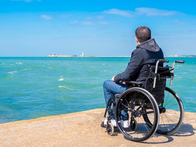 Hintergrundansicht eines Mannes, der am Ufer gegen den Himmel sitzt