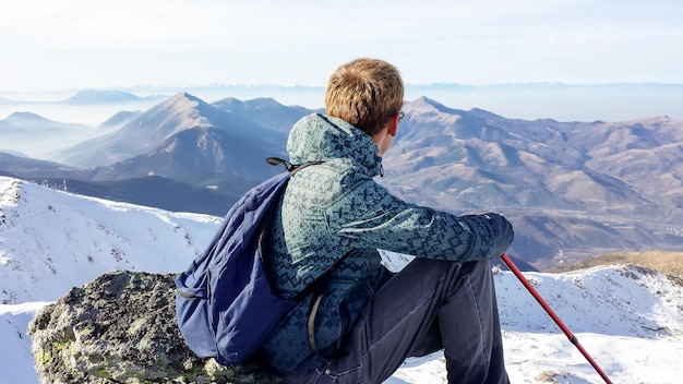 Hintergrundansicht eines Mannes, der auf einem Felsen auf einem Berg sitzt