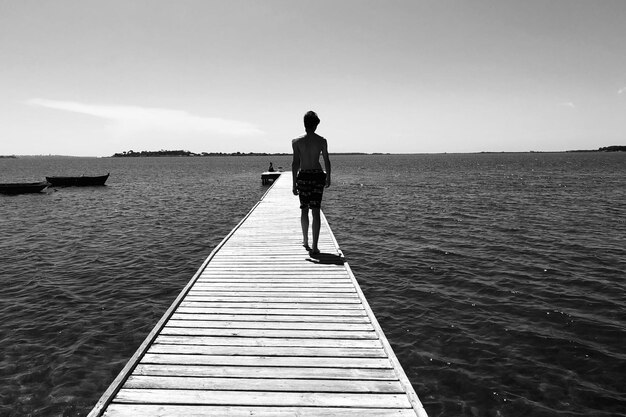 Foto hintergrundansicht eines mannes, der auf einem pier über dem meer gegen den himmel geht