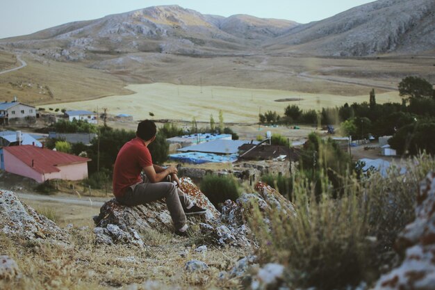 Foto hintergrundansicht eines mannes, der auf einem see gegen berge sitzt