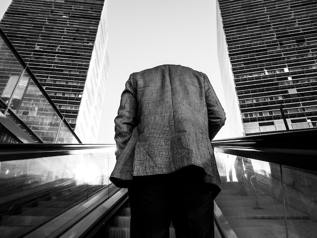 Hintergrundansicht eines Mannes, der auf einer Rolltreppe gegen den Himmel steht