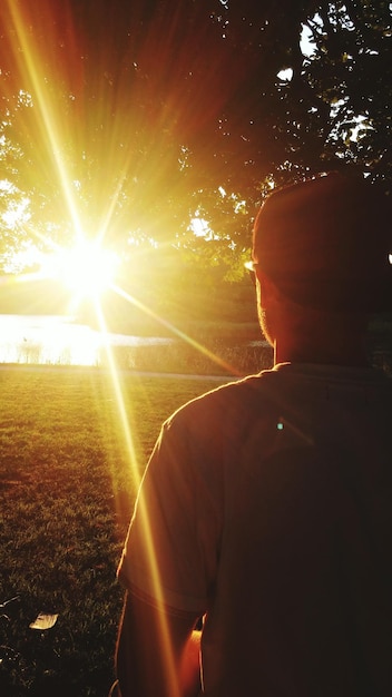 Foto hintergrundansicht eines mannes, der bei sonnenaufgang auf dem feld gegen die sonne steht