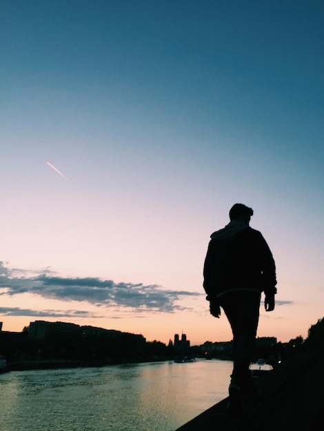 Hintergrundansicht eines Mannes, der bei Sonnenuntergang gegen den Himmel geht