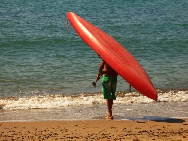 Foto hintergrundansicht eines mannes, der ein rotes kanu am ufer am strand trägt