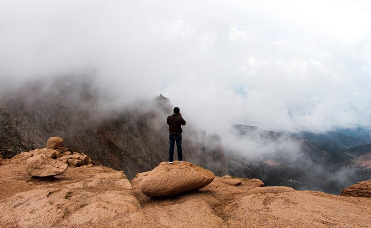 Foto hintergrundansicht eines mannes, der eine berglandschaft gegen einen bewölkten himmel fotografiert