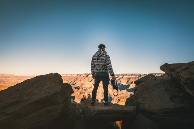 Foto hintergrundansicht eines mannes, der eine kamera hält, während er auf einem felsen gegen den himmel steht