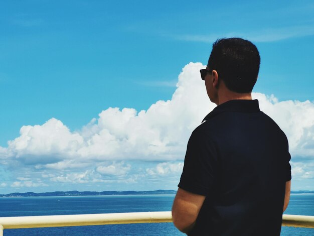 Hintergrundansicht eines Mannes, der gegen einen bewölkten Himmel auf das Meer schaut