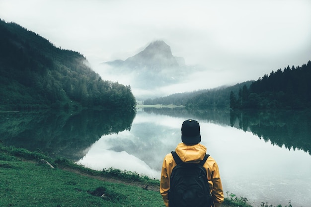 Foto hintergrundansicht eines mannes, der im nebligen wetter am obersee-see bei den bergen schaut