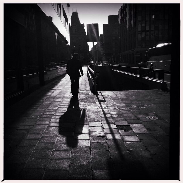 Foto hintergrundansicht eines mannes, der mit schatten auf einem fußweg in der stadt geht