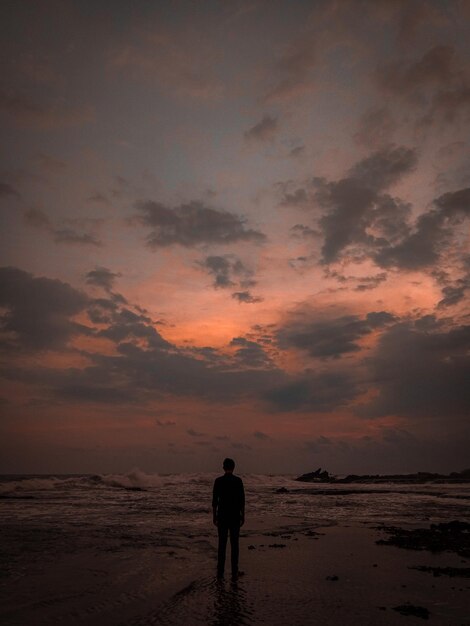 Hintergrundansicht eines Mannes, der während des Sonnenuntergangs am Strand gegen den Himmel steht