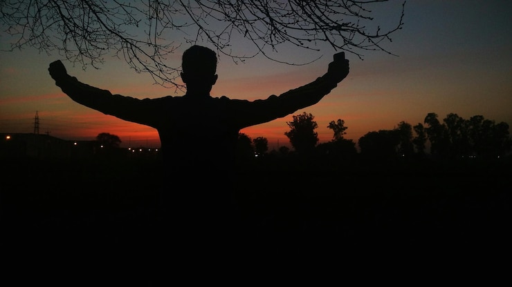 Foto hintergrundansicht eines mannes mit ausgestreckten armen, der bei sonnenuntergang gegen den himmel steht