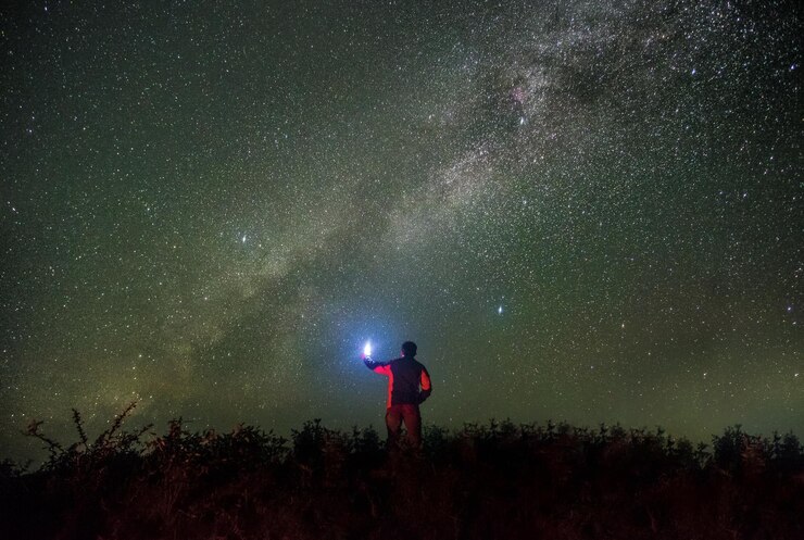 Foto hintergrundansicht eines mannes mit beleuchteter taschenlampe, der gegen das sternenfeld steht