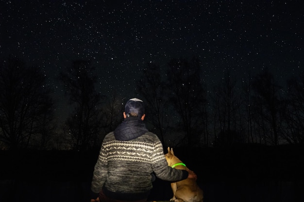 Foto hintergrundansicht eines mannes mit hund im wald gegen das sternenfeld bei nacht