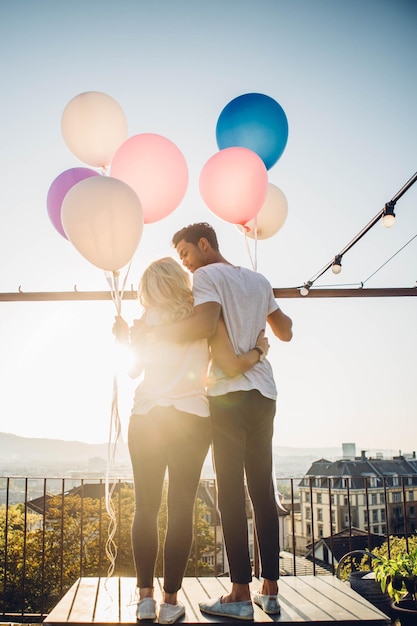 Hintergrundansicht eines Paares, das mit Ballons gegen den Himmel steht