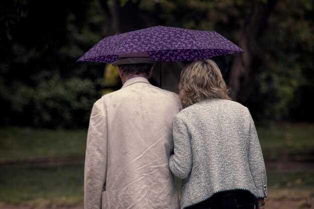 Foto hintergrundansicht eines paares, das unter einem regenschirm im park spazieren geht
