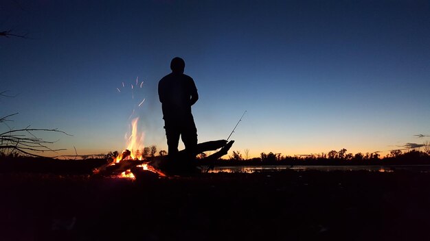 Foto hintergrundansicht eines silhouettenmannes, der vor einem lagerfeuer gegen einen klaren himmel steht