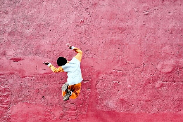 Hintergrundansicht eines spielerischen Jungen, der gegen eine alte rote Wand springt