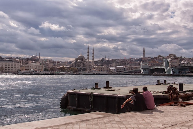 Hintergrundansicht von Freunden, die am Hafen bei Moscheen in der Stadt gegen einen bewölkten Himmel sitzen