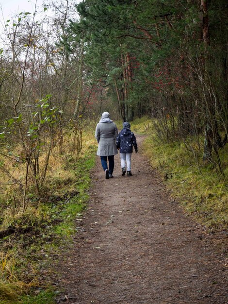 Foto hintergrundansicht von mutter und tochter, die auf dem pfad zwischen den bäumen im wald spazieren gehen