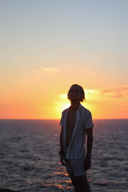 Hintergrundbeleuchtetes Porträt eines jungen Mannes im Vintage-Stil bei Sonnenuntergang auf dem Meer