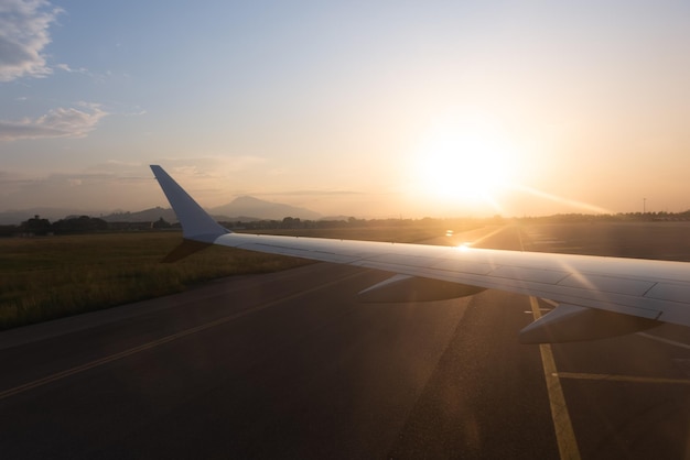 Hintergrundbeleuchtung des linken Flügels des Flugzeugs auf der Landebahn bei Sonnenuntergang am Berg bis zum Horizont