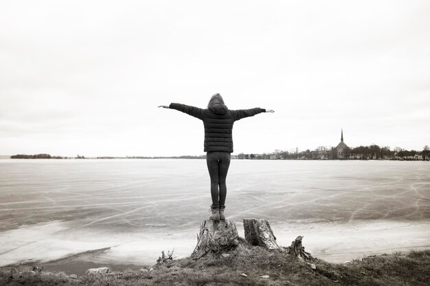 Hintergrundbild in voller Länge einer Frau mit ausgestreckten Armen, die am gefrorenen See steht