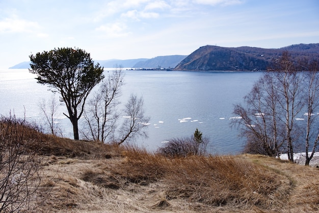 Hintergrundlandschaftsansicht des Baikalsees mit Bäumen und Bergen im April bei Kamen Cherskogo, Oblast Irkutsk, Russland