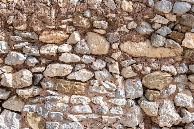 Hintergrundtextur der Felsmauerkonstruktion Alte graue, beige, raue Steinmauer mit Zement