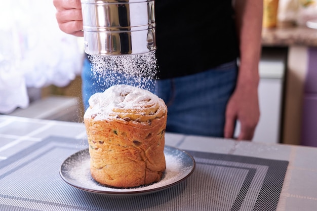 Hinzufügen von Zuckerpulver auf leckeren Osterkuchen auf einem Teller