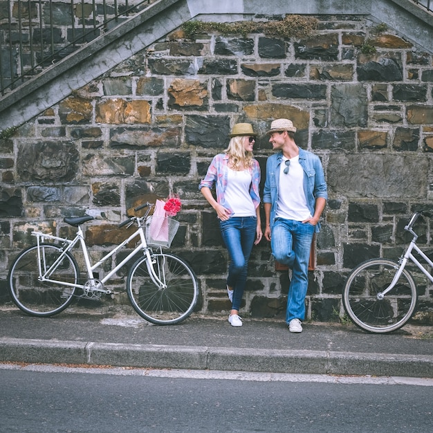 Hip jovem casal de pé na parede de tijolos com suas bicicletas