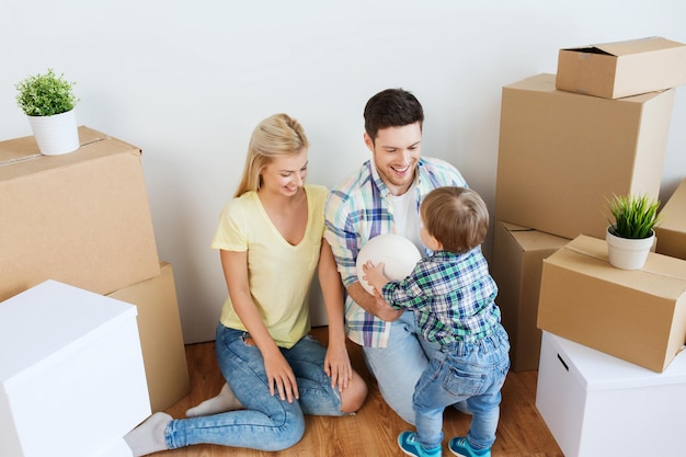 Hipoteca, gente, vivienda, mudanza y concepto inmobiliario - familia feliz con cajas jugando a la pelota en un nuevo hogar