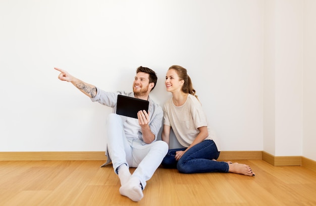 Foto hipoteca, personas y concepto de bienes raíces - pareja feliz con tablet pc en la habitación vacía de la nueva casa